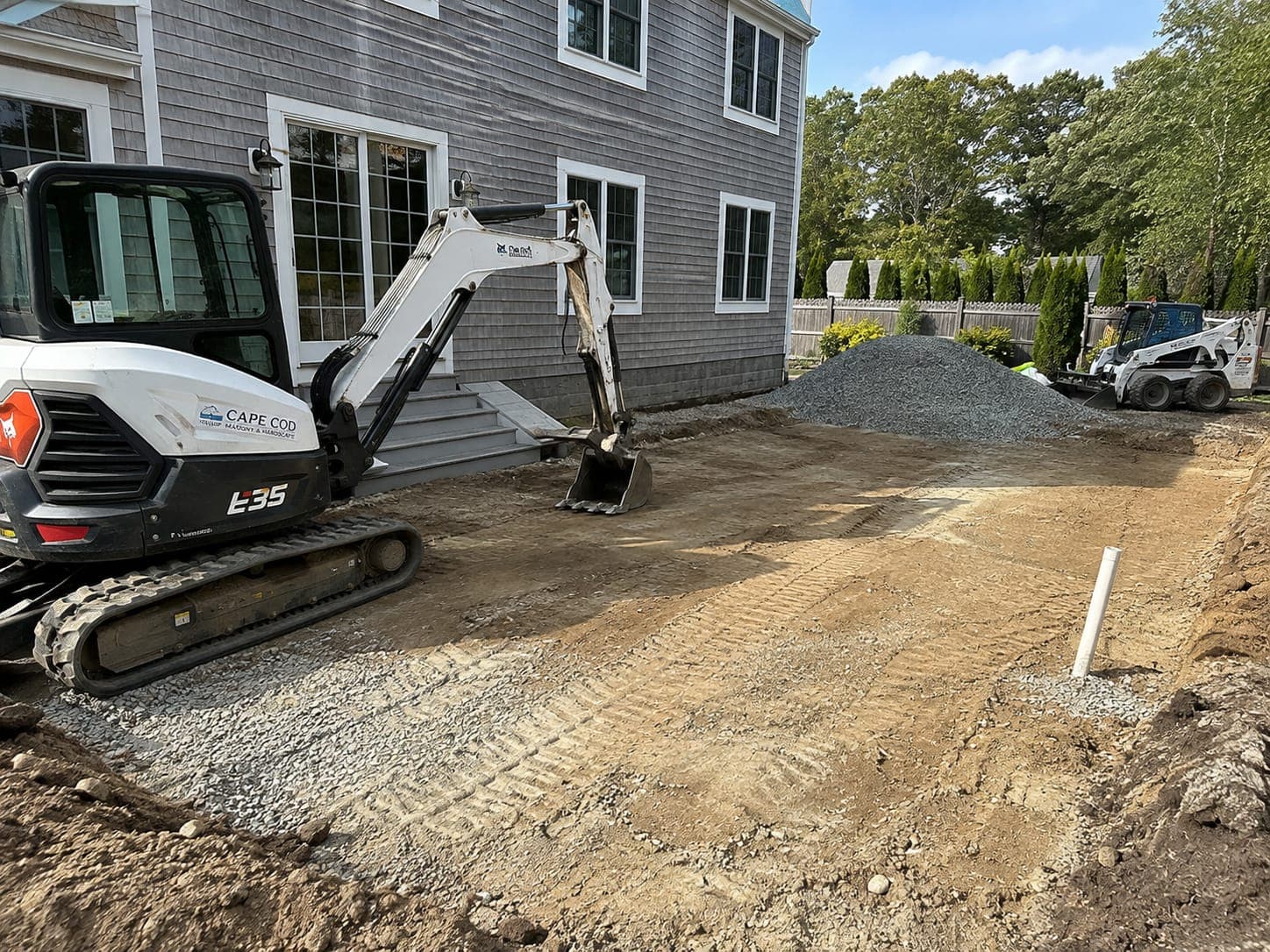 Excavadora compacta rompiendo un patio de concreto agrietado en el patio trasero de una vivienda en Cape Cod