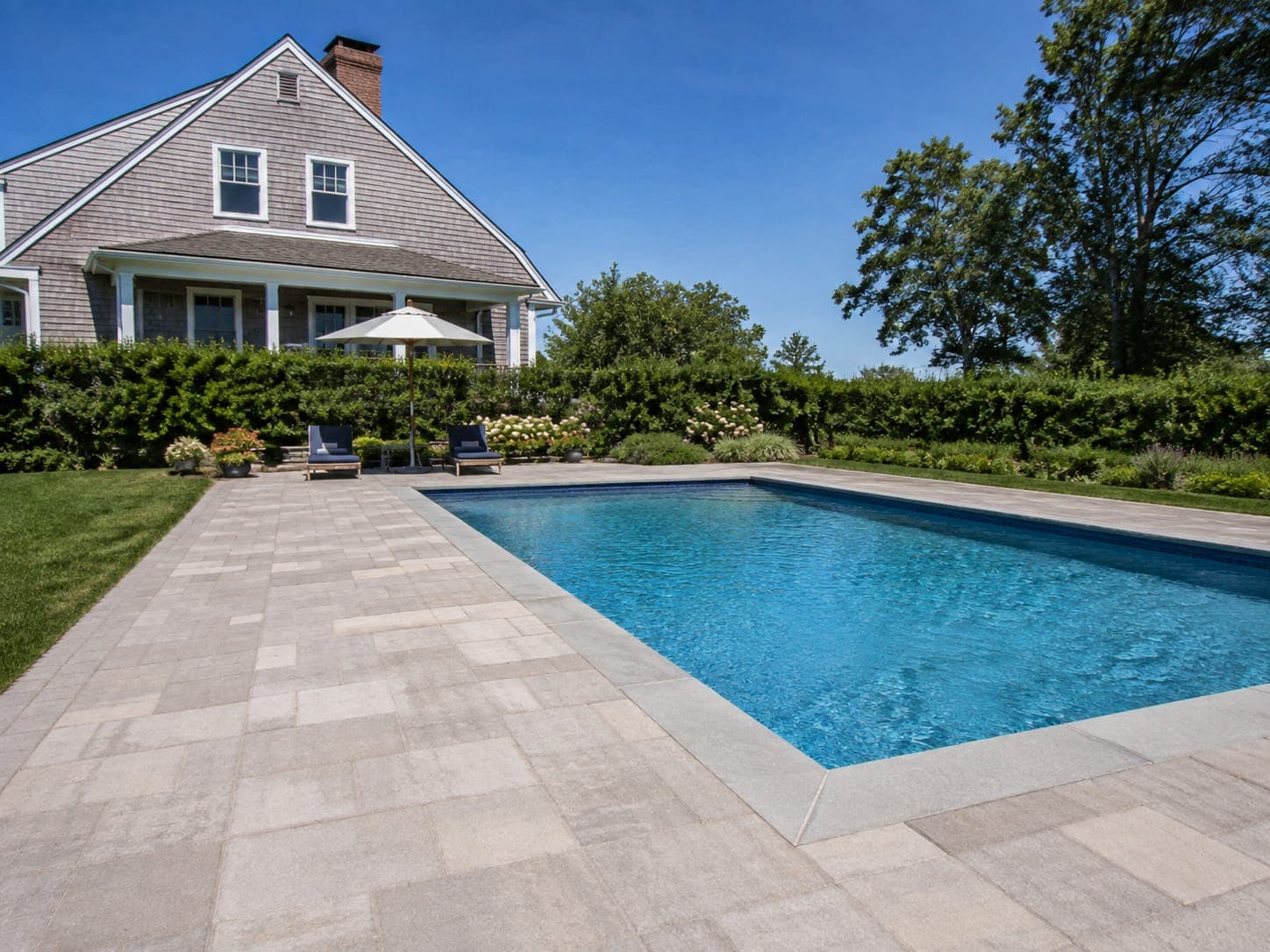 In-ground pool with wide bluestone coping, paver pool deck and a low stone seat wall in a Cape Cod backyard