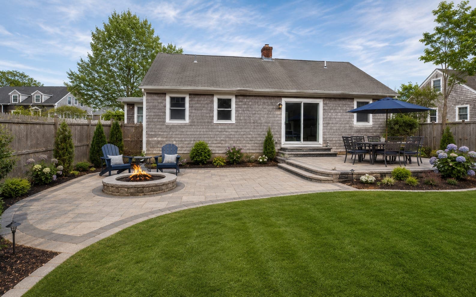 The same backyard after construction with a new paver patio, stone seat wall and fresh plantings