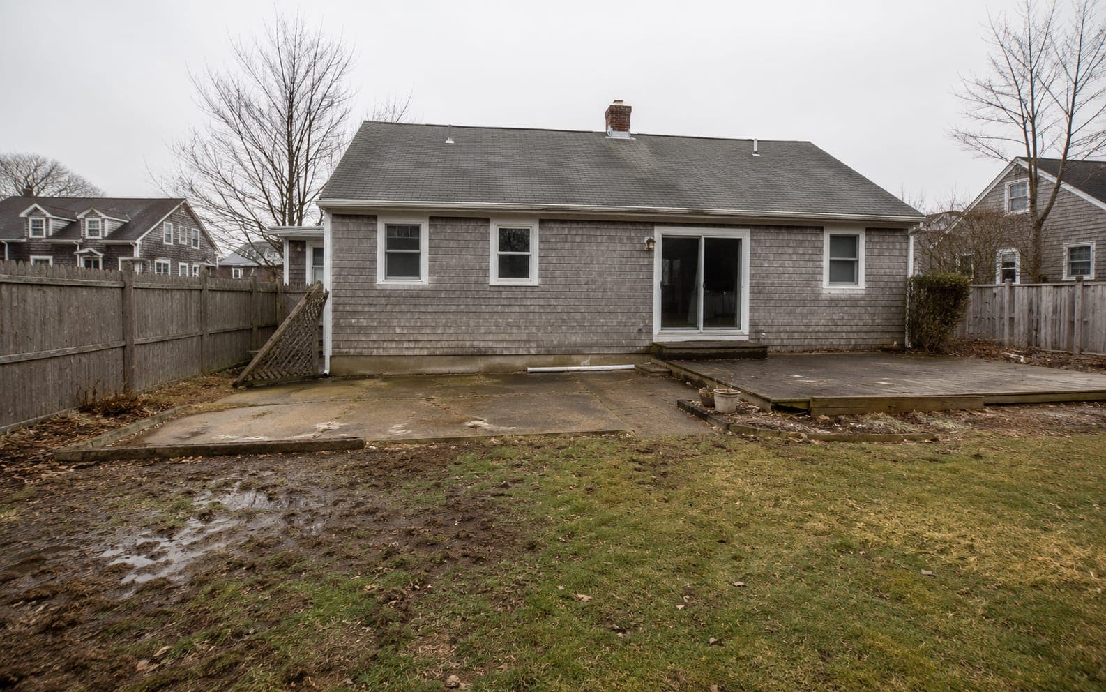 Backyard before renovation with a cracked, sunken concrete patio and patchy lawn